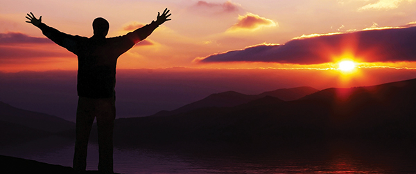 man looking at sunset with arms outstretched