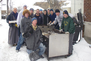 LOMBARDO and some winter-hardy volunteers take a break from hauling the old damaged stove out of the rectory to make way for a new one.