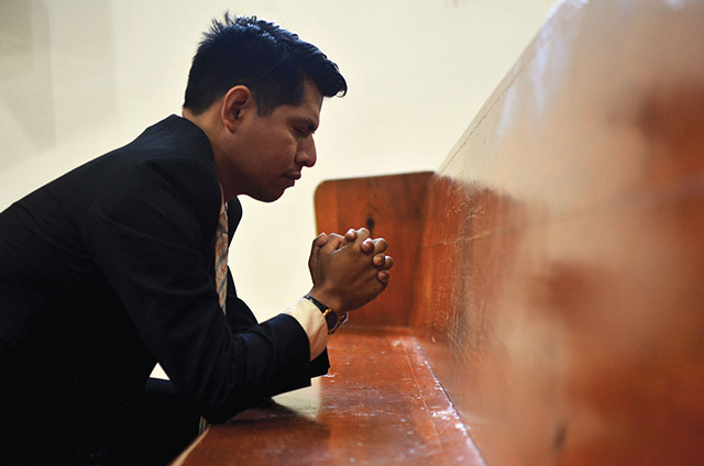 young man kneeling in a church pew praying