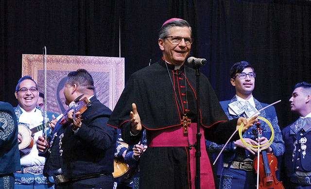 García-Siller comparte el escenario con una banda de mariachis en una reunión de la arquidiócesis.