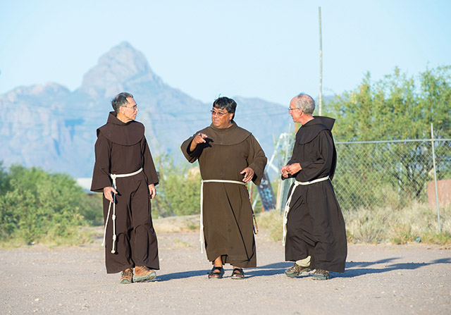 Friars David Paz, O.F.M. (left), Father Ponchie Vásquez, O.F.M. (center), and Peter Boegel, O.F.M. (right) take an evening walk with the sacred mountain Baboquivari in the distance.