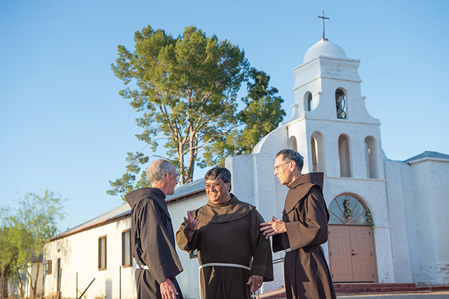 Father Ponchie Vásquez, O.F.M. chats in front of the church in Topowa, Arizona with Friars Peter Boegel, O.F.M. (left) and David Paz, O.F.M. 