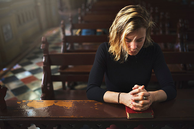 Young woman praying while kneeling in a church