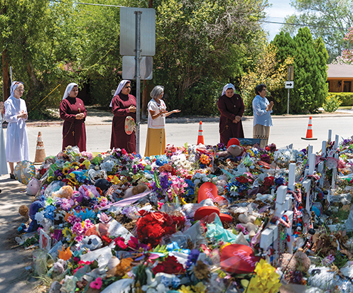 Sisters stand in prayer in front of the flowers and other tributes piled up in the Robb Elementary schoolyard. 