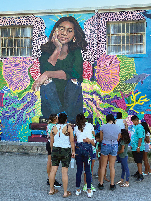 A group views a mural of one of the children who died during the school shooting in Uvalde, Texas in May 2022. The child’s mother receives a hug.