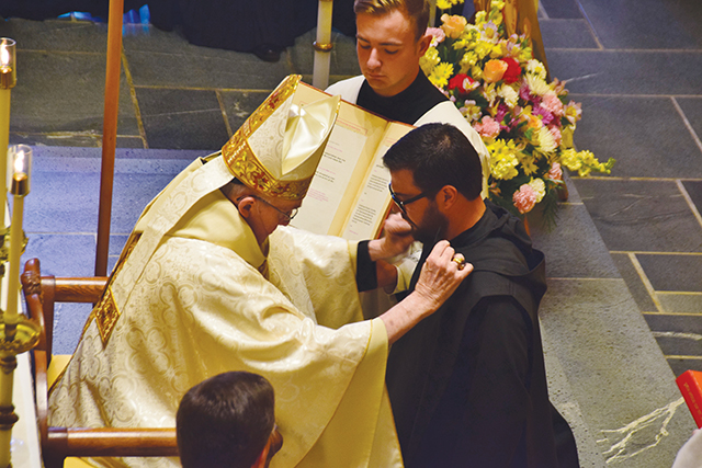 The abbot of the monastery places the hood, or capuche, around the shoulders of Brother Pachomius Alvarado, O.S.B. during his profession of temporary vows. 