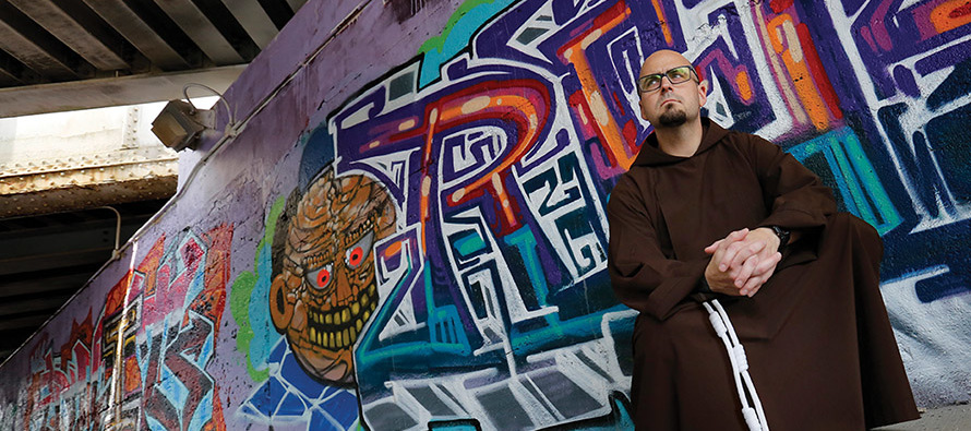 Father M.J. Groark, O.F.M.Cap. sits in front of a wall of graffiti