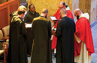Monks chant at St. Bernard Abbey, two wearing the red vestments of priests (alb, stole, and chasuble) while the others wear the black monastic habit.