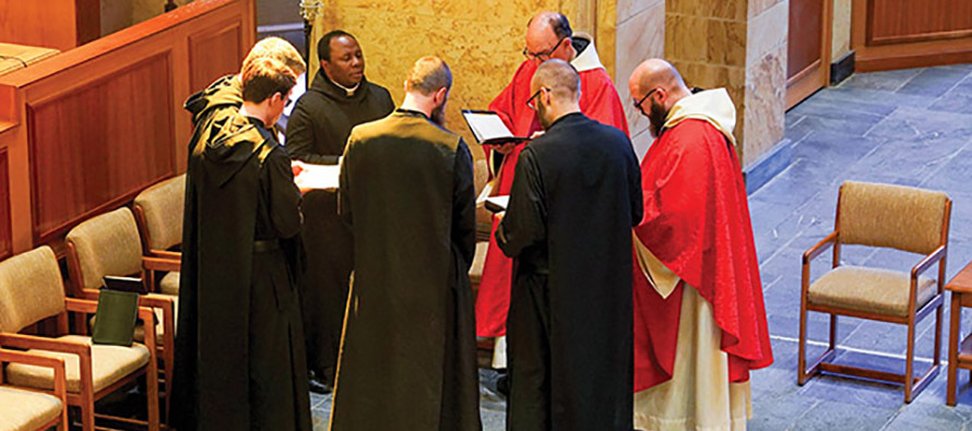 Monks chant at St. Bernard Abbey, two wearing the red vestments of priests (alb, stole, and chasuble) while the others wear the black monastic habit.